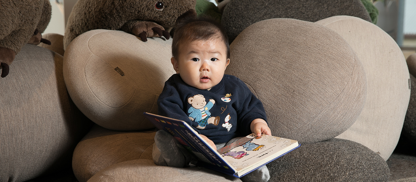 Small child sat on stuffed pebbles reading a board book.