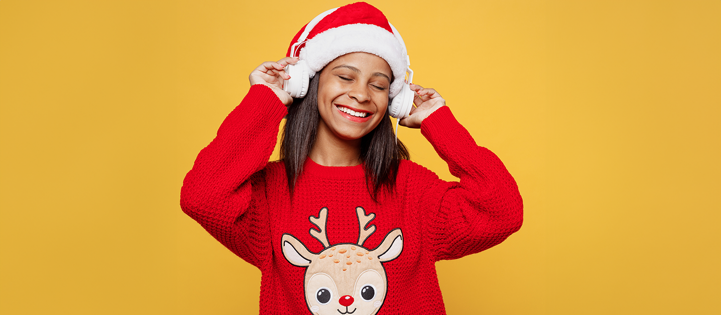 Young woman in Santa Hat and red reindeer jumper listening to music through headphones. 