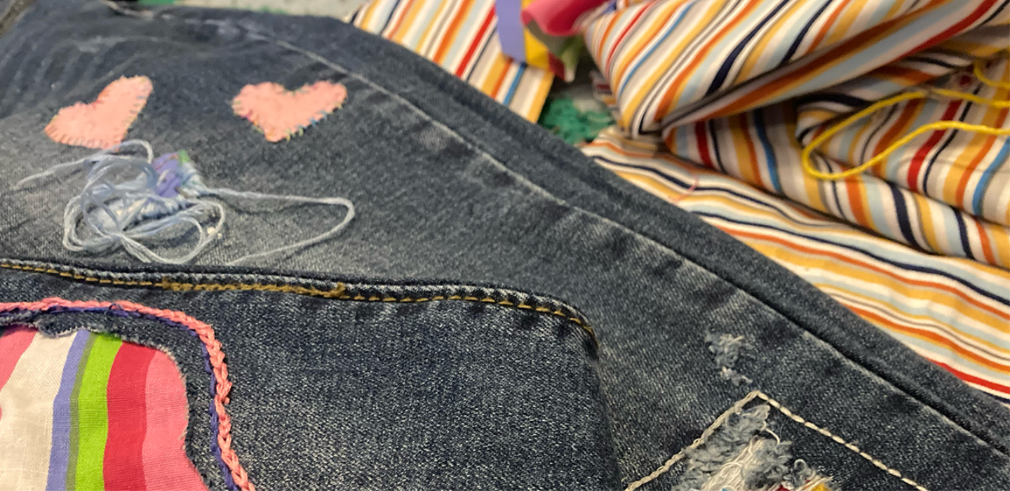 Brightly coloured visible mending on denim jeans.