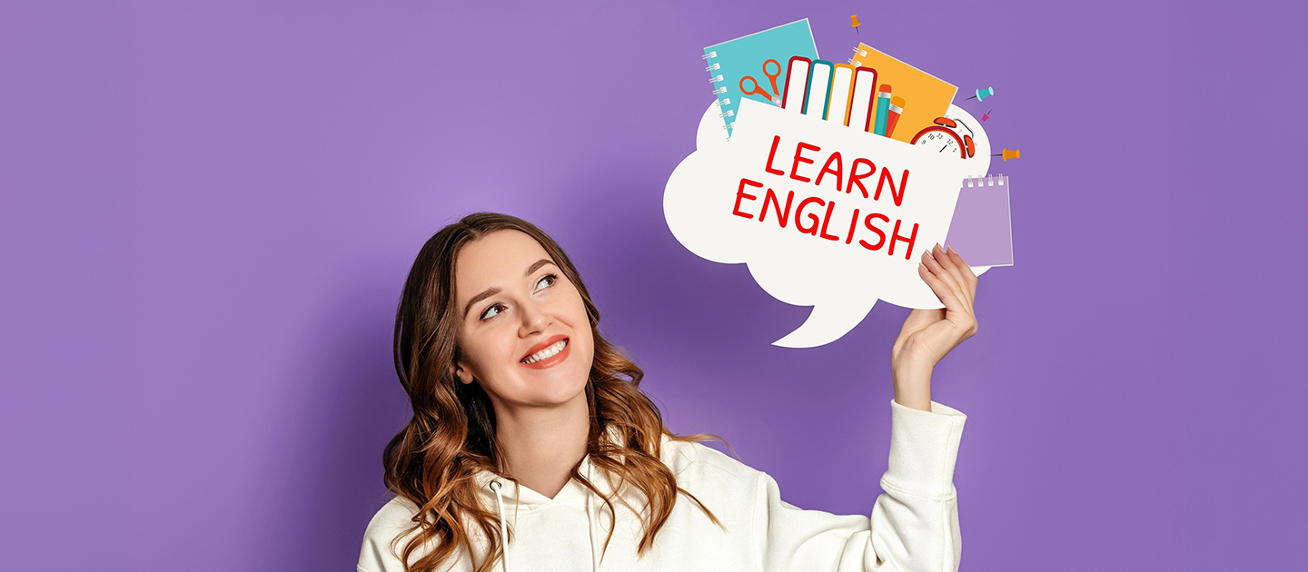Young female student in cream hoody holding up a learn English speech bubble