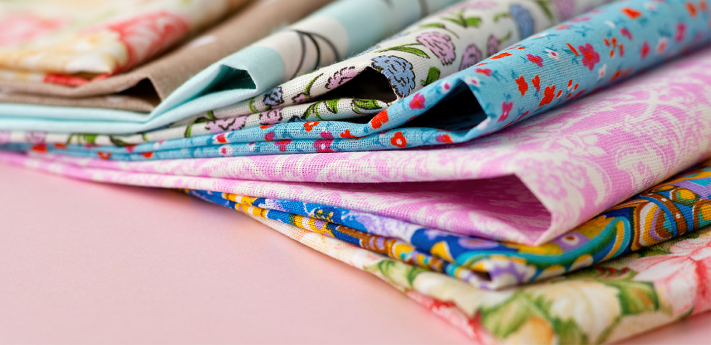 Brightly coloured folded patterned cloth laid out on a pink background.