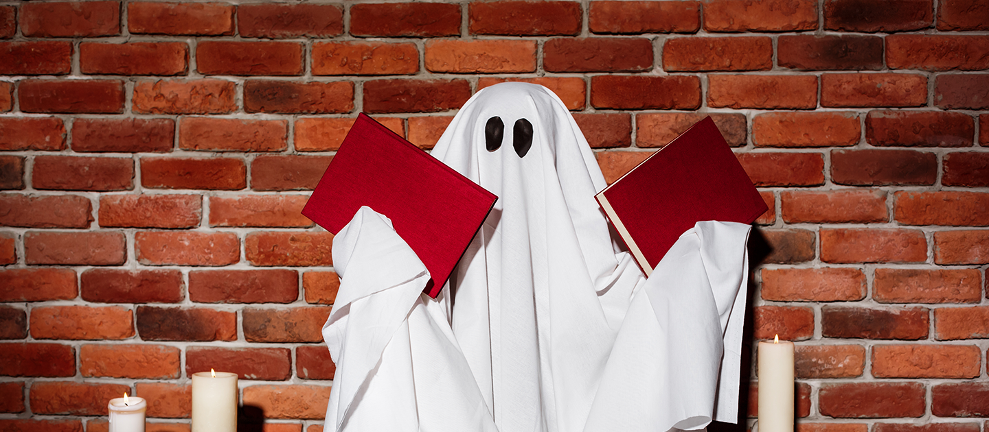Person wearing a sheet ghost costume and holding books. 