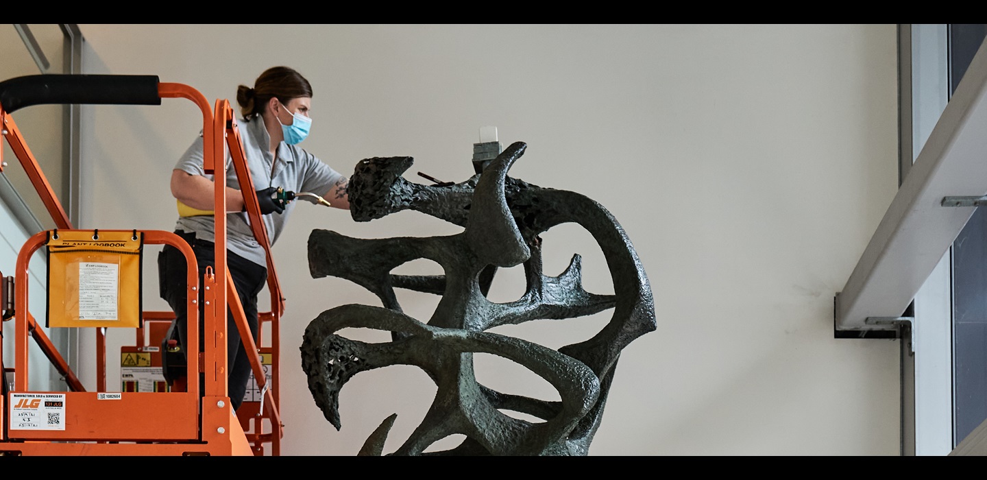 Conservator Claire Rowson working on a cherry picker at the top of a tall sculpture.