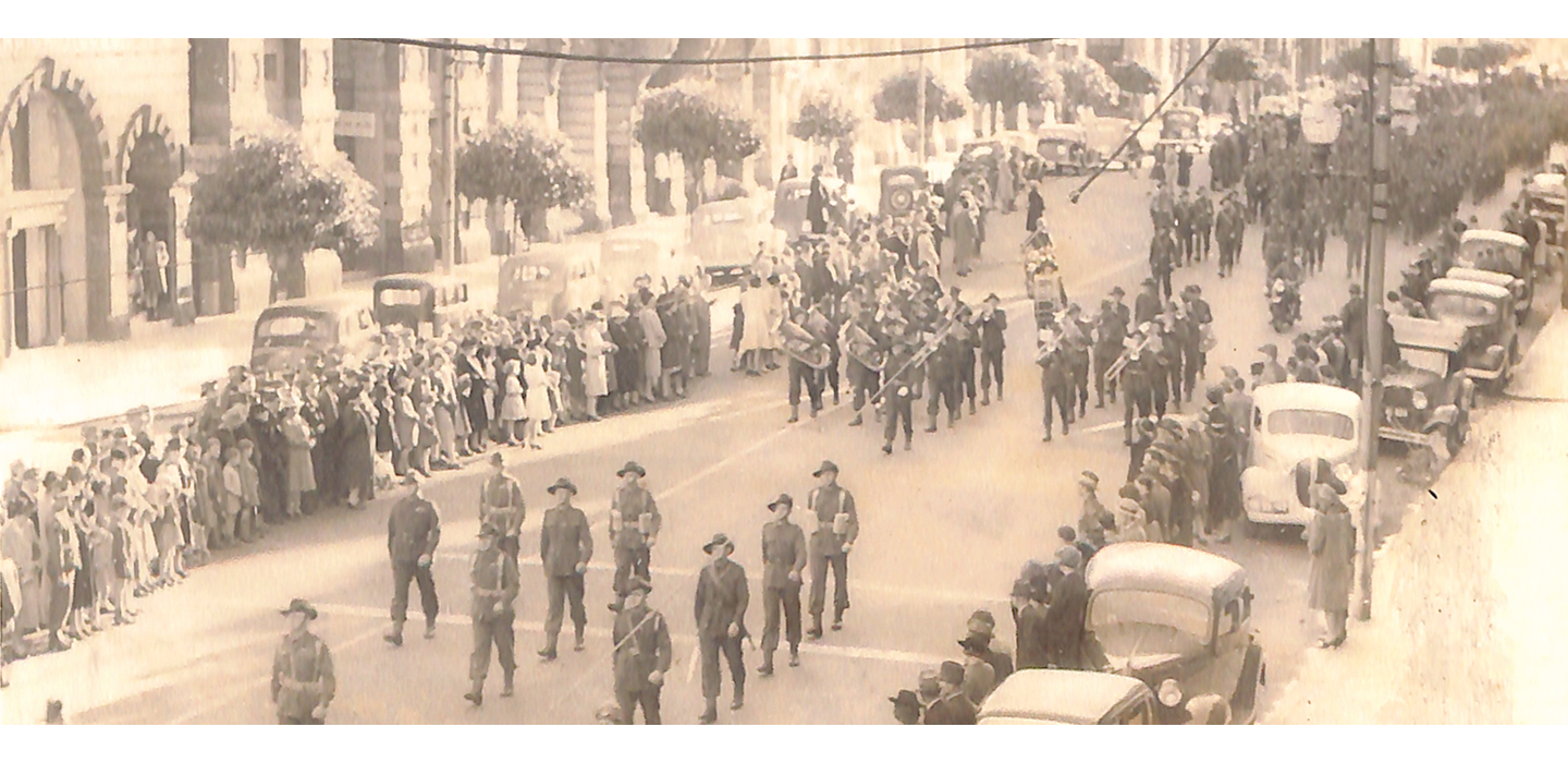 Old sepia photograph of a military parade progressing down a street.