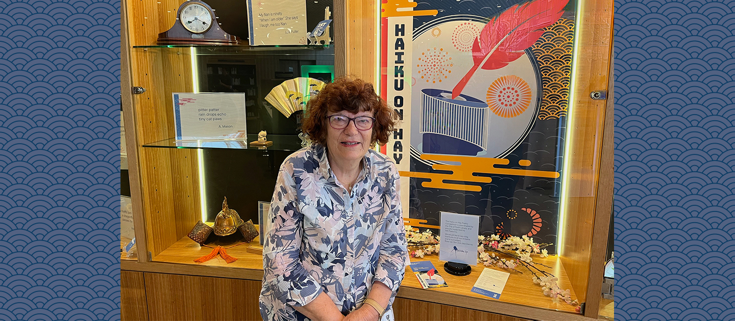 Photo of poet and writer Rose van Son sitting in front of the Haiku on Hay display at the Library.