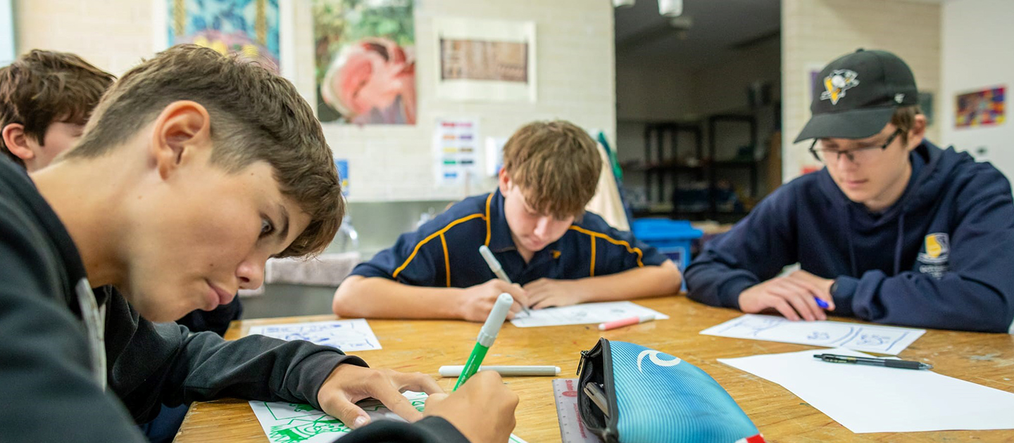 Students in uniform sat around a table, producing artwork.
