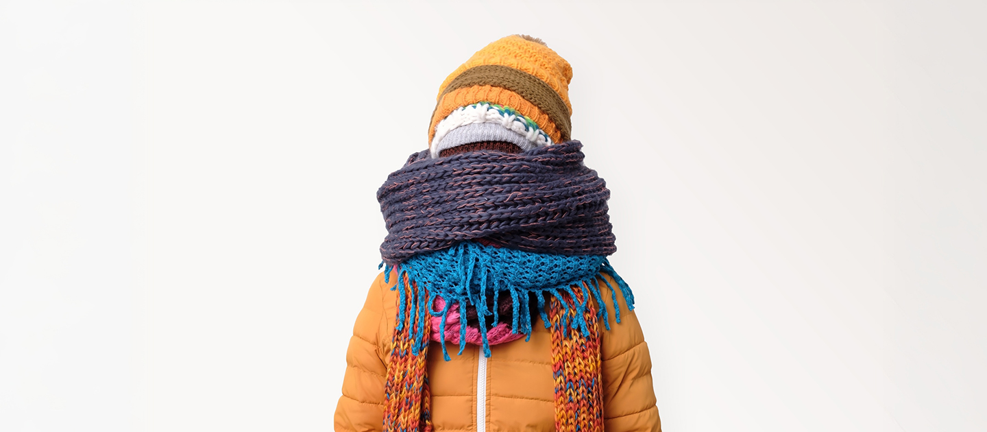 Man bundled up in a coloured jacket with multiple scarves and hats.
