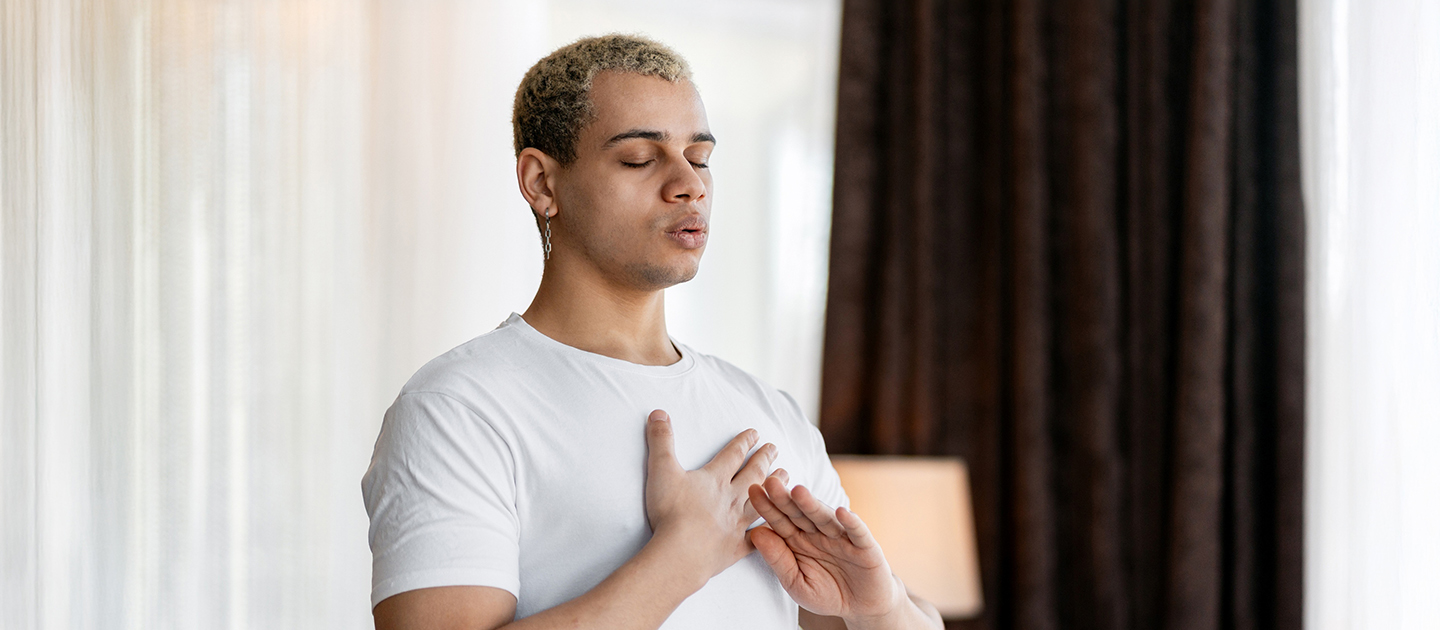 Young man with eyes shut and hands on chest doing breathing exercises.