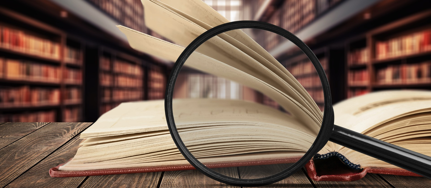 Magnifying glass in front of a book, with a library background.