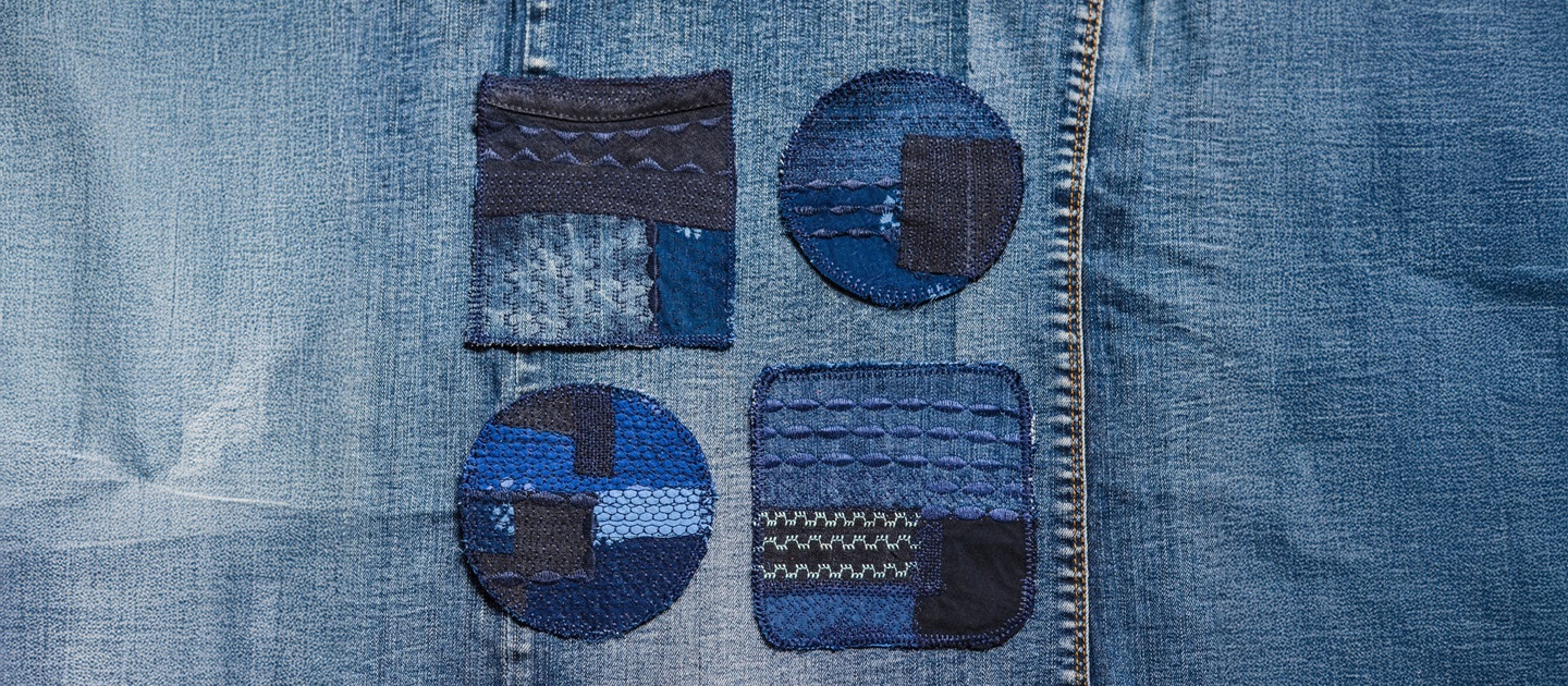 Indigo and blue visible mending patches with intricate stitching on dark blue denim.