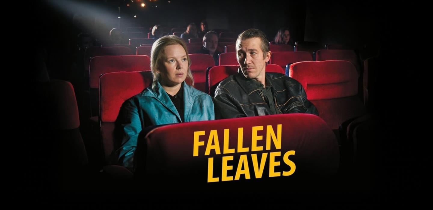 Film promotion for Fallen Leaves, woman and man sat in a dark cinema on red seats.