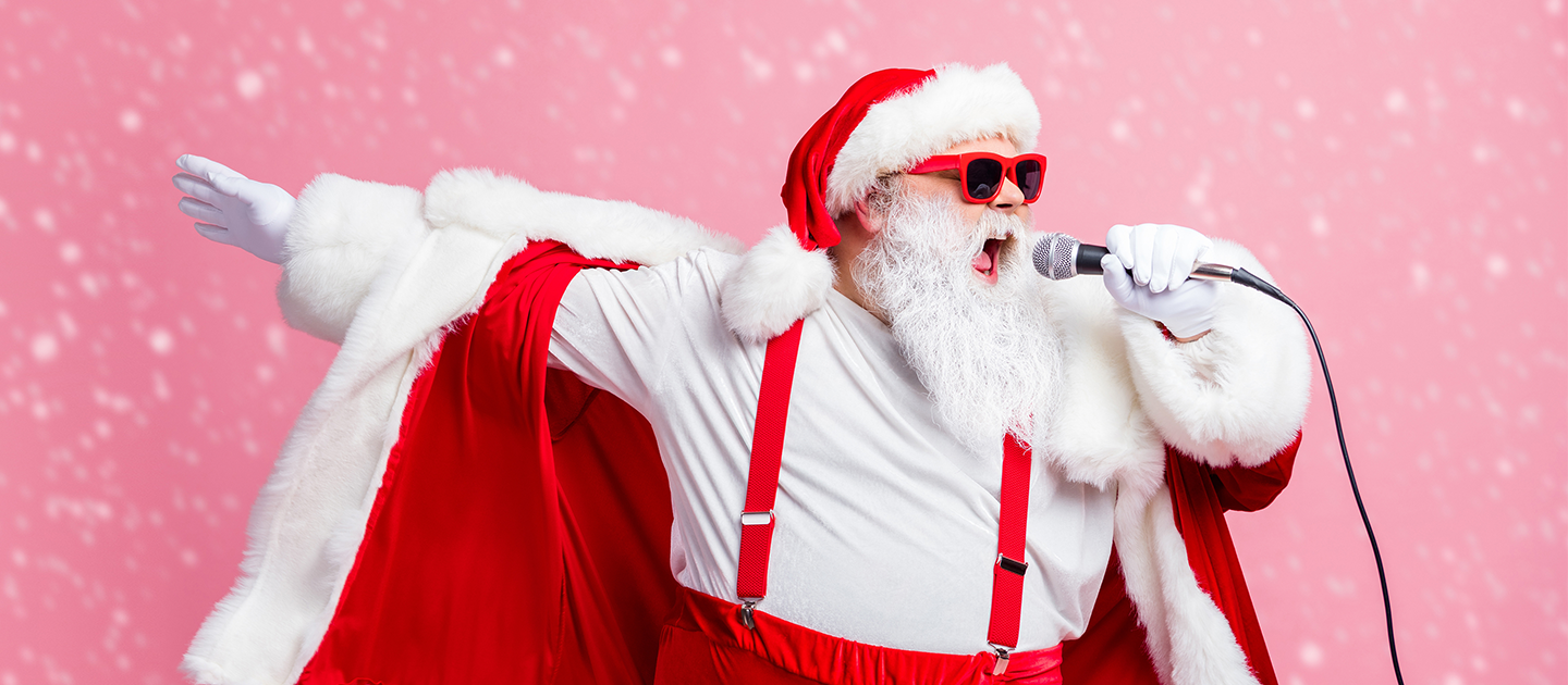 Man dressed as Santa singing a rocking song into a handheld microphone. 