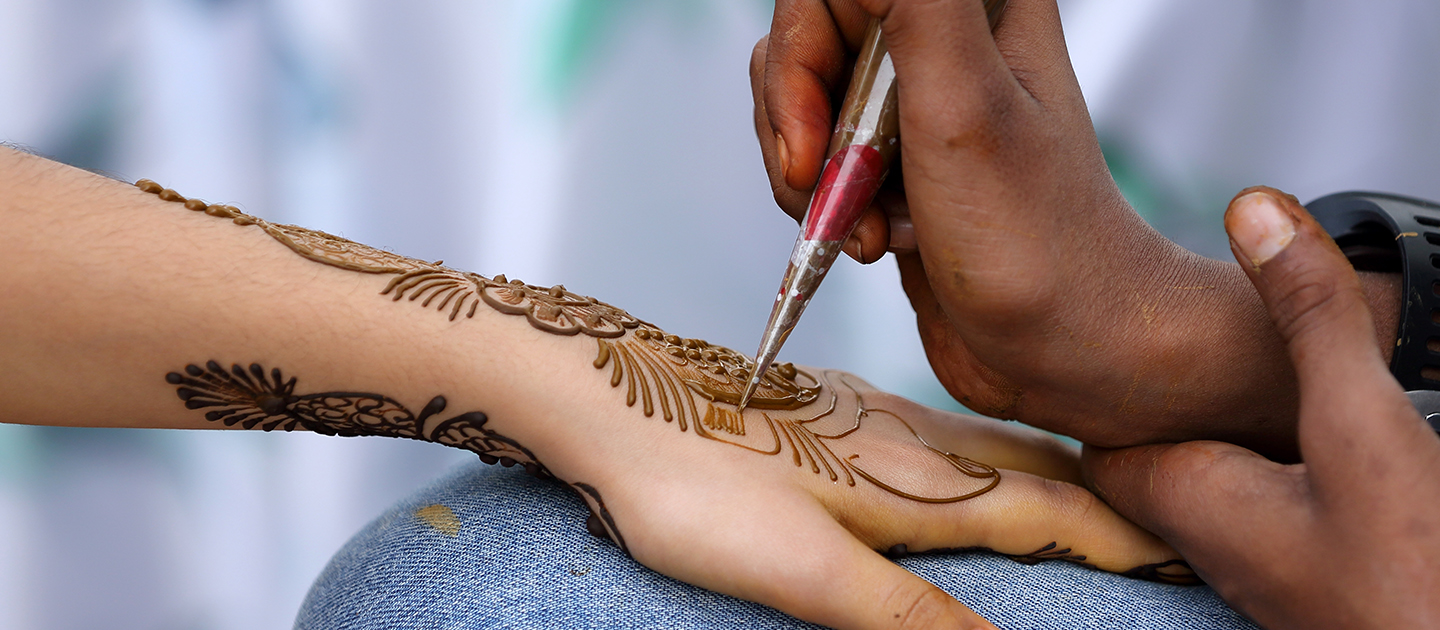 Close up of Henna artist painting an intricate design on a woman's hand.