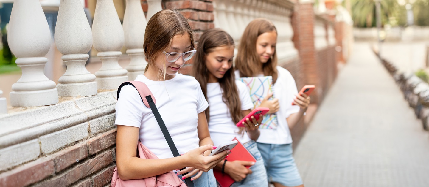 Three teenage girls leaning against a brick wall looking at their phones