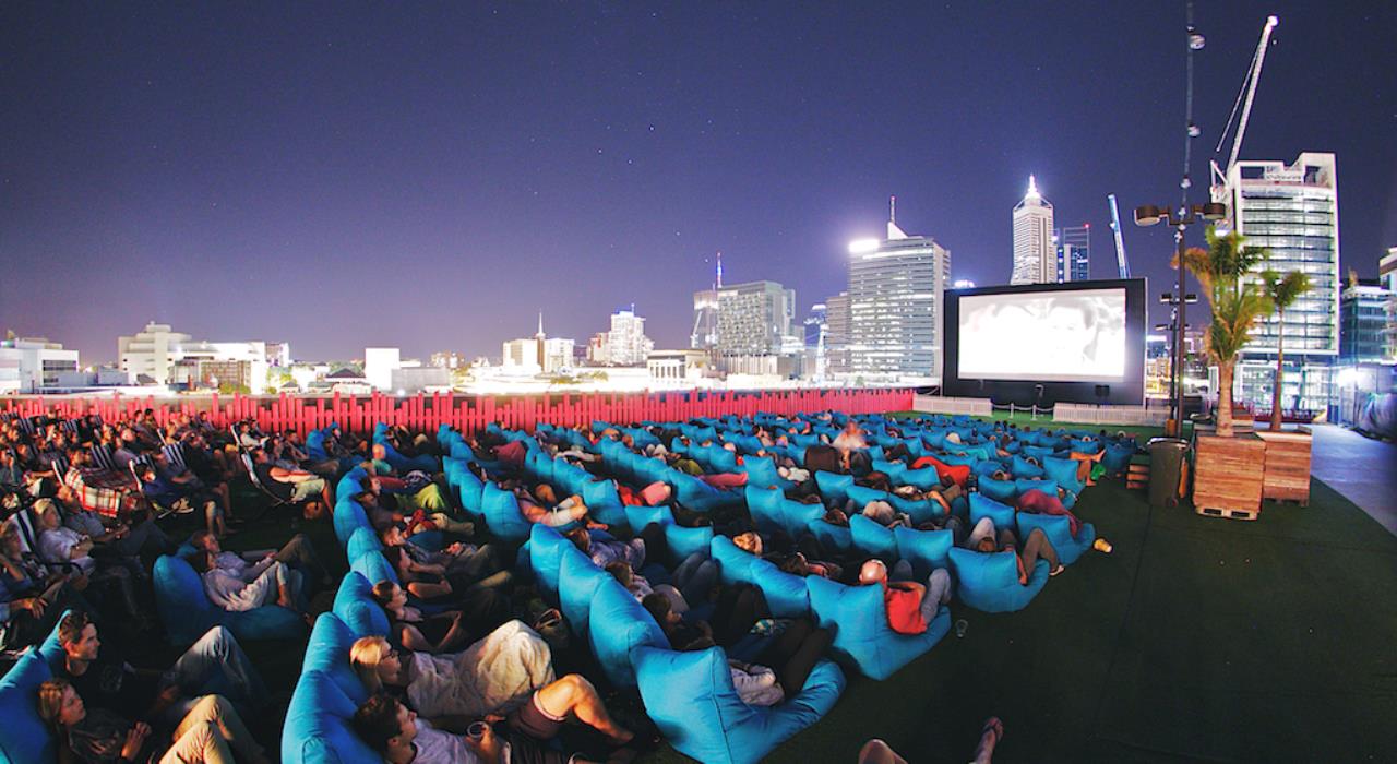 View of audience watching movie on rooftop with City in background