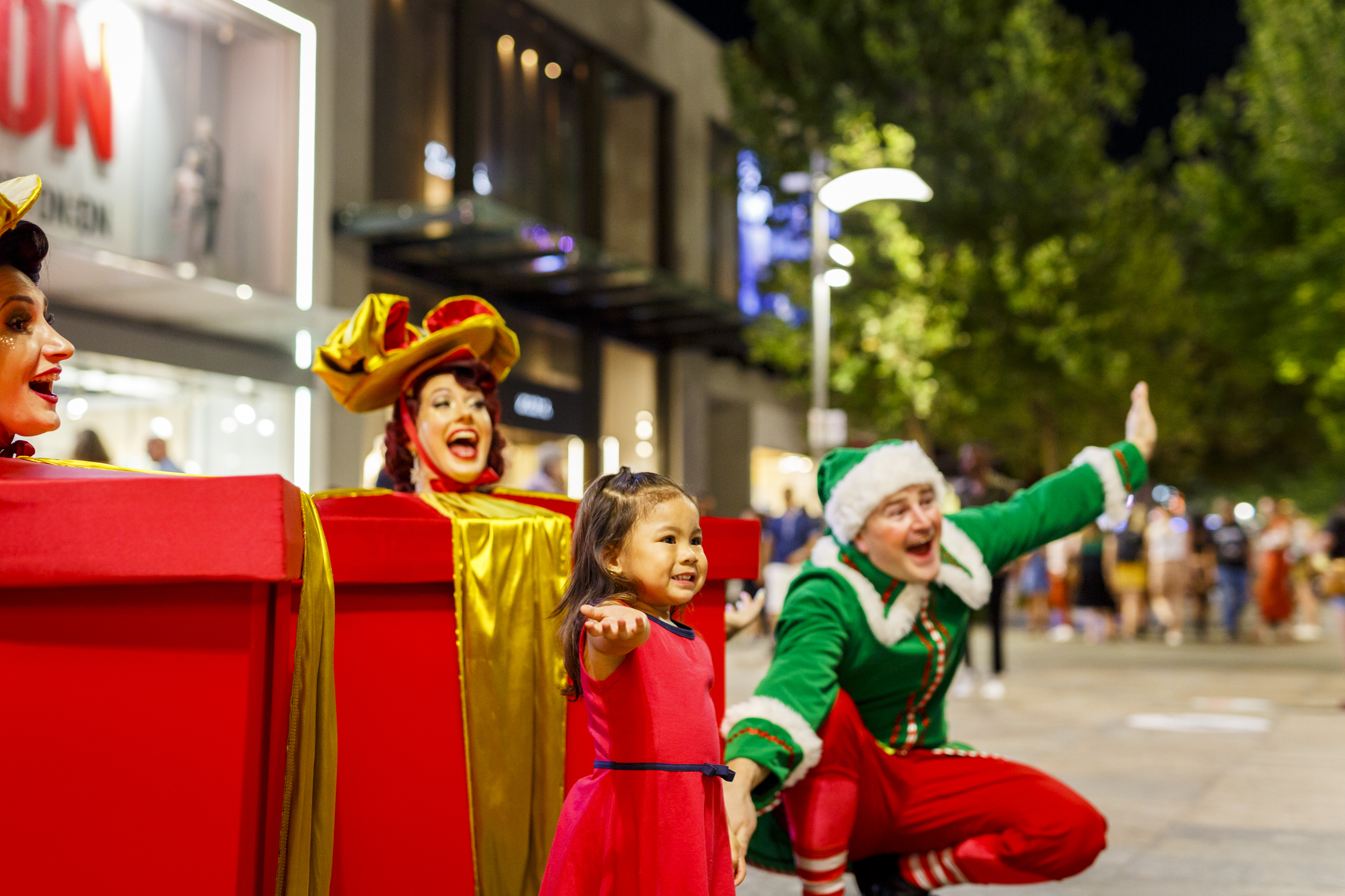 Elf and small child stand in front of large presents