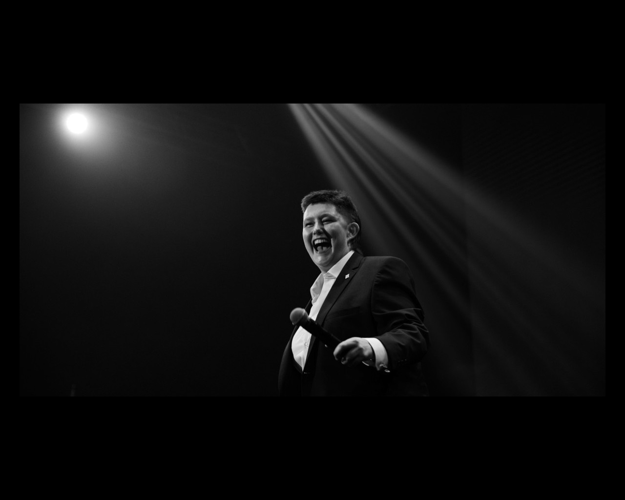 Black and white photo of Alissia Marsh in a suit on stage holding a microphone