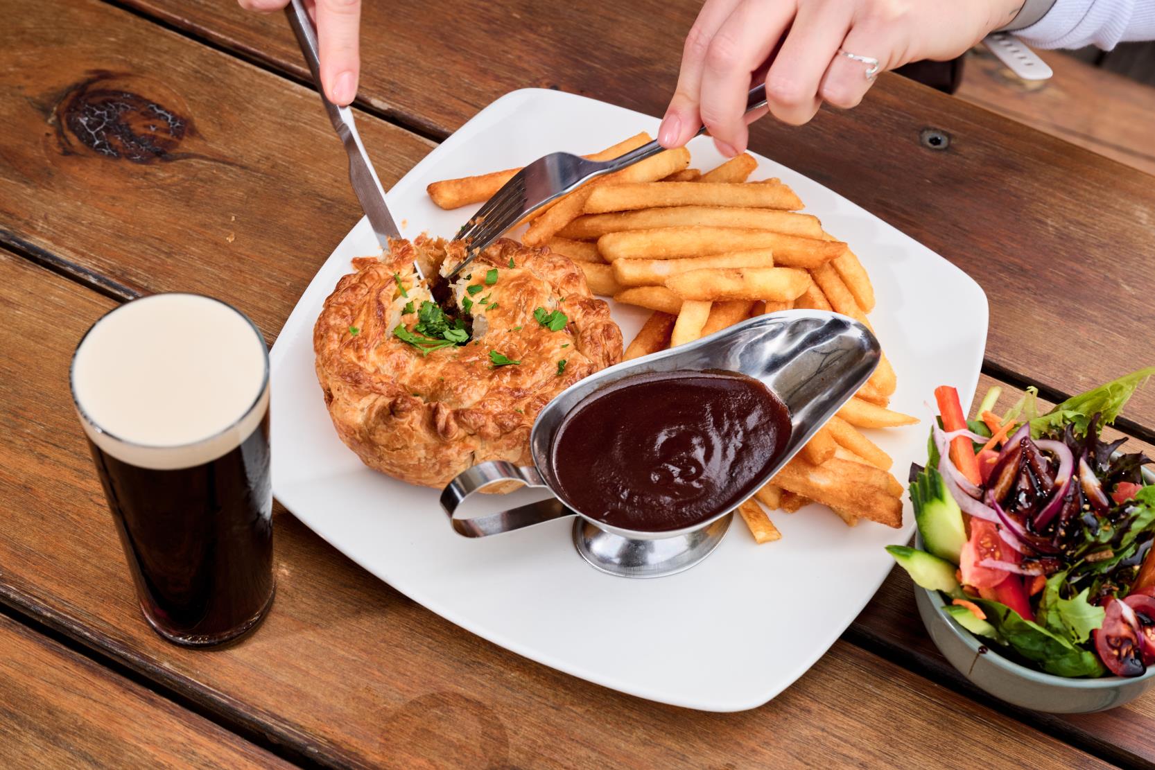 person cutting into pie with chips, gravy, salad and guinness